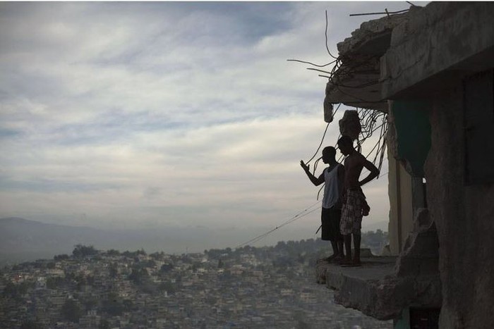 Hai người đàn ông đứng trên tấm sàn bê tông nhô ra từ ngôi nhà bị mất một nửa sau trận động đất kinh hoàng ở Haiti. Tác giả: Allison Shelley.
